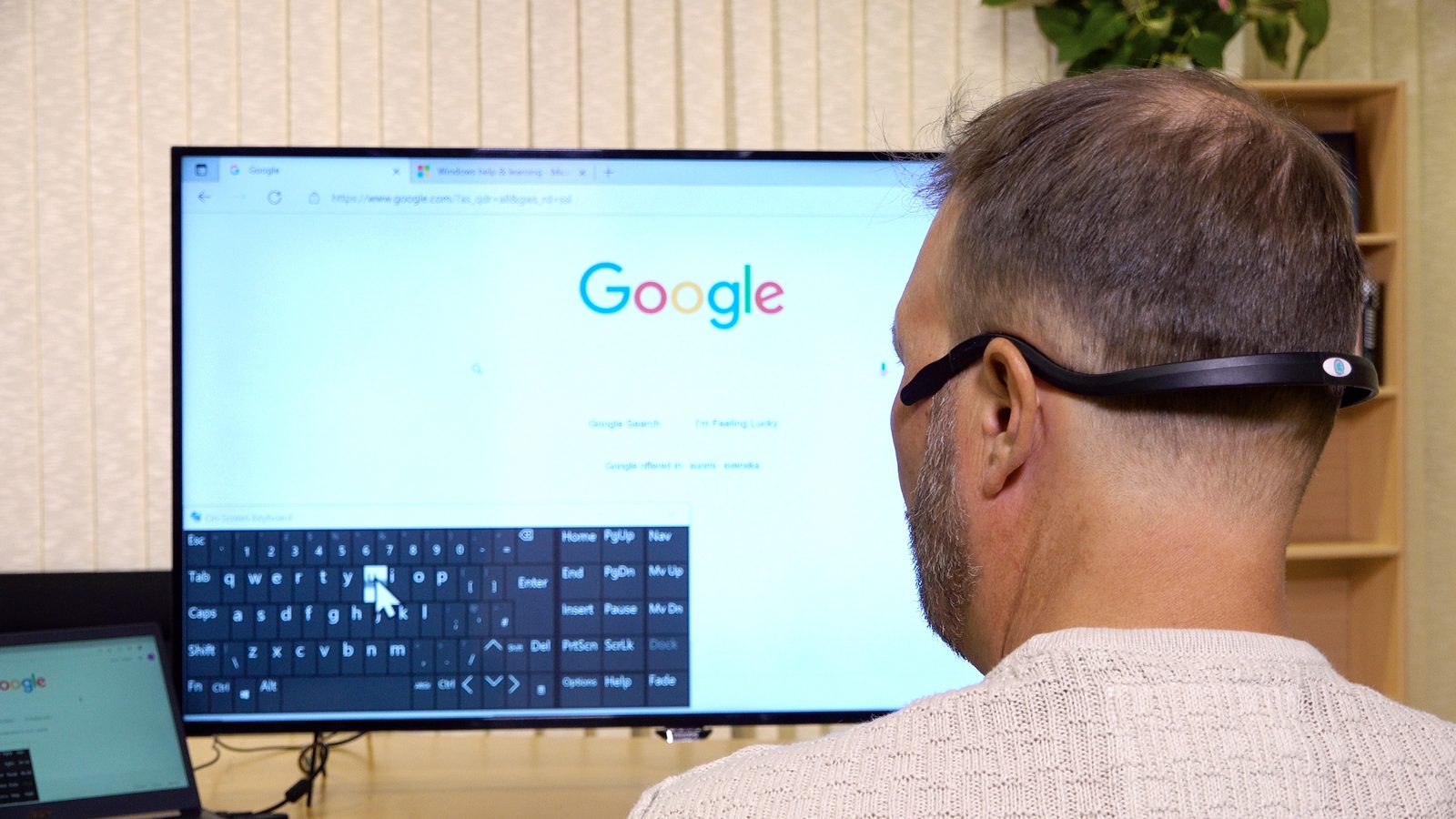 Ein Mann bedient seinen Computer mit der Quha-Kopfmaus und einer Bildschirmtastatur
